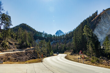 Mountain road through forested valley with steep descent sign..