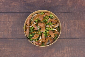 A bowl of food with a sauce on top. The bowl is brown and has a green and white color