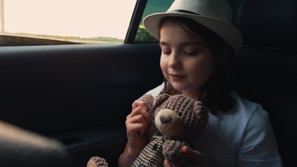 The child holds the bear. The child looks out the window. The car drives on the road. The child's hand touches the bear with one hand car keeps going. holidays van ride summer road, school holidays