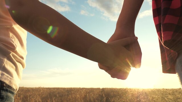 two hands holding each other against sunset, mother child holding hands sunset, happy family, adult child hand symbolize care, closeness trust between parent child, against background field golden