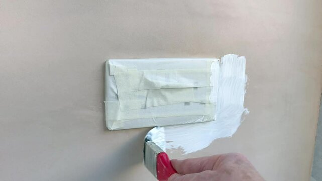 Coat of plaster priming paint being brushed around an electrical socket which has been taped up to protect it from paint. No people. DIY concept.