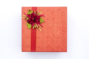 A red box decorated with roses and a red ribbon. This box is used as a container for wedding souvenirs.