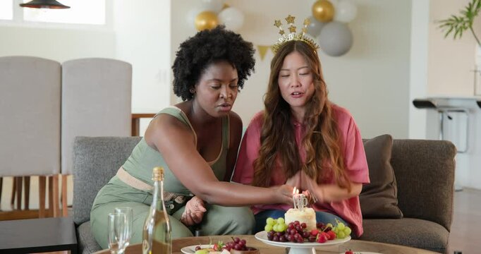 African American, Asian friends celebrating 30th birthday in living room, sharing cake and bubbly