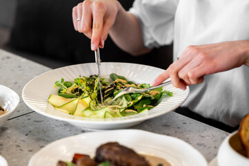 A plate of fresh salad with leafy greens, cucumber slices, and creamy dressing, presented alongside a fork and knife, emphasizing healthy dining and nutrition.