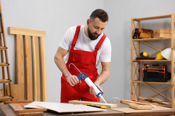 Worker with caulking gun glueing wooden plank indoors
