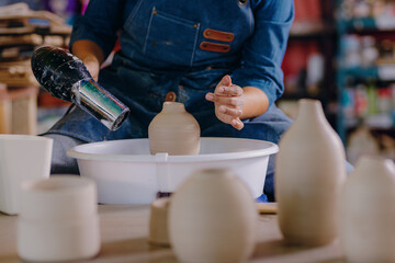 Young Mexican woman, 24, uses a hairdryer to dry a ceramic piece. The close-up highlights the precision and care in her hands during the process.
