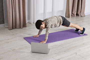 Little boy exercising near laptop at home. Morning routine