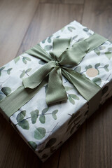 Beautifully wrapped gift in a paper with eucalyptus and a green bow. Wrapping paper with green eucalyptus on white background.