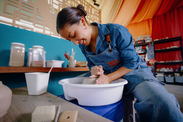Mexican woman, 24, molds a ceramic piece in her studio wearing a blue apron, shirt, and jeans....