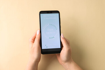 Menstruation. Woman holding smartphone with period calendar application on beige background, top...