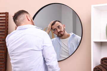 Fototapeta premium Baldness problem. Man with receding hairline near mirror in bathroom