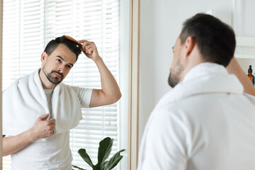 Fototapeta premium Handsome man styling his hair with comb near mirror at home
