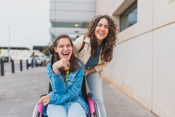 Young woman with cerebral palsy laughs with her personal assistant outdoors - They share a candid...