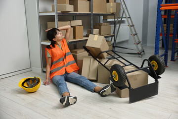 Accident at work. Injured woman and overturned hand truck on floor in warehouse