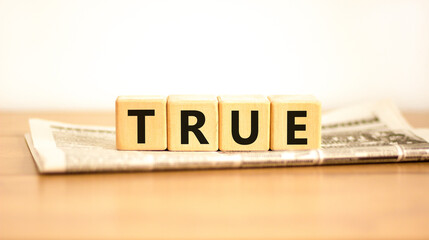 True symbol. Concept word True on beautiful wooden blocks on newspaper. Beautiful wooden table...