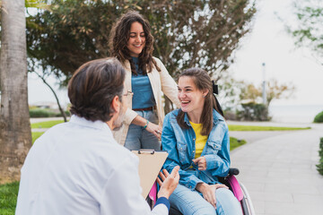 Smiling doctor talking to young woman in wheelchair and caregiver - Happy young woman with cerebral...