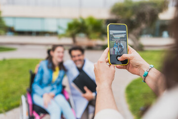 Caregiver taking photo of doctor and young woman in wheelchair - Close-up of smartphone capturing smiling doctor with young woman with cerebral palsy - Concept of cerebral palsy