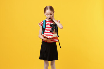 Schoolgirl with backpack reading book on yellow background