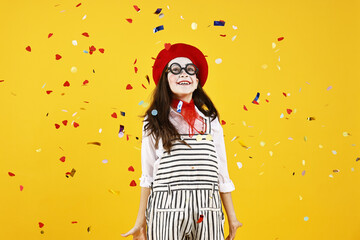 Happy girl dressed like mime under falling confetti on yellow background. Surprise party