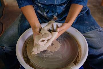 Mexican woman, 24, molds a ceramic piece in her studio, wearing a blue apron and denim. Close-up on her hands.
