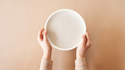 Hunger concept. Woman holding empty plate waiting for food. Top view