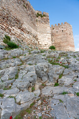 A detailed view of an ancient stone fortress wall featuring two crenellated towers. The rugged...