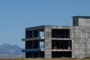 Construction of a modern building structure against a clear blue sky and mountain backdrop in late afternoon sunlight