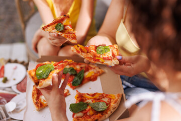 Hands grabbing fresh pizza slices outdoors, close-up of group enjoying meal together.