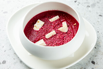 A vibrant bowl of beetroot soup garnished with cream and fresh herbs, served on a modern white plate, adding a touch of elegance to any dining experience.