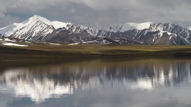 Drone captures majestic snow-covered mountains and a lake on the Arabel Plateau in Kyrgyzstan, showcasing natural beauty.