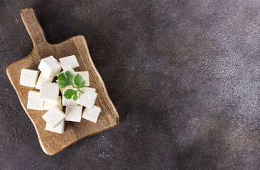 Cubes of Indian paneer cheese on a wooden board on a gray background. Indian food. Top view. Copy...