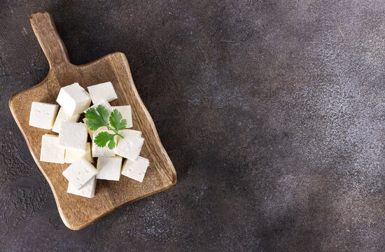 Cubes of Indian paneer cheese on a wooden board on a gray background. Indian food. Top view. Copy space.