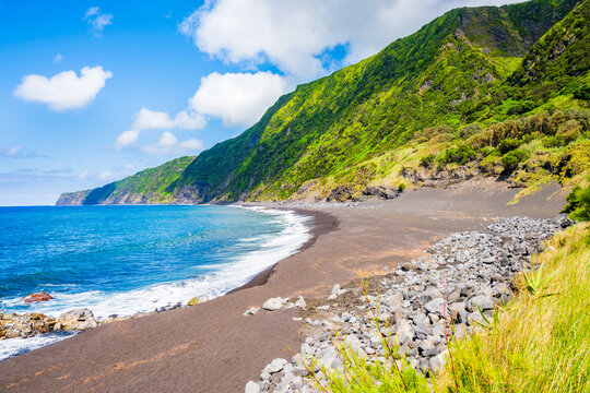 Black sand volcanic beach of Faja and green tropical landscape with high cliffs on ocean coast, Faial island, Azores, Portugal