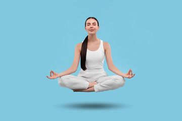Young woman levitating during meditation on light blue background. Practicing yoga
