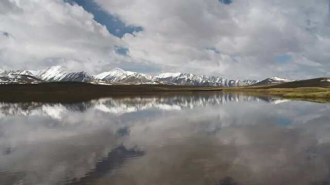 Beautiful drone footage captures reflections of snow-covered mountains and clouds on a lake at Arabel Plateau.