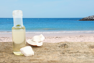 Cooking oil in glass bottle and coconut pieces on wooden table against beach. Space for text