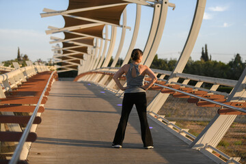 Active middle-aged woman doing stretching and jogging outdoors at sunset