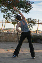 Active middle-aged woman doing stretching and jogging outdoors at sunset