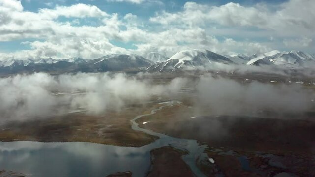 4K drone flies through moving clouds over lakes and snowy peaks on the Arabel Plateau during mixed weather.