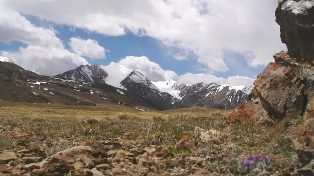 Timelapse video of clouds drifting over a meadow surrounded by snowy mountains at Arabel Plateau.