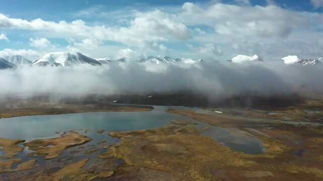 Cinematic 4K drone footage of Arabel Plateau and Barskoon Valley, Kyrgyzstan, captures a flight through foam-like clouds and over snowy mountains lit by sunshine.