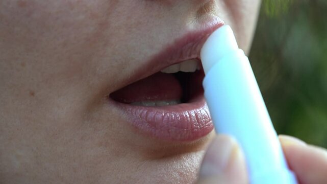 Careful woman applying moisturizing lipstick in delicate slow motion, protecting and nourishing dry lips with cosmetic skincare treatment