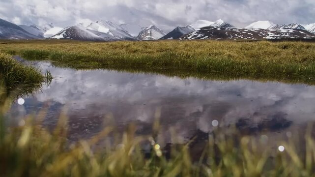 A breathtaking panoramic 4K shot of Arabel Valley, Kyrgyzstan, where the green meadows surround a reflective lake, with sunshine illuminating snowy peaks and clouds overhead