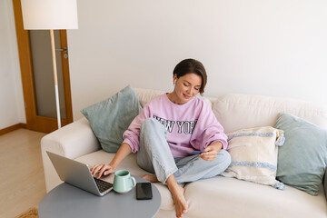 young attractive woman sitting at home on sofa working on laptop