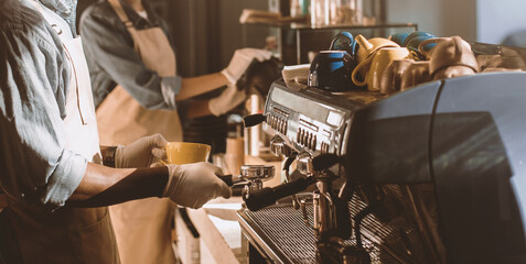 Preparing takeaway coffee during covid-19 and social distancing. Couple of busy young african american barista in aprons, protective masks and gloves work with professional equipment in cafe, cropped