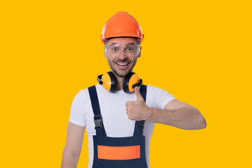 Builder engineer isolated on yellow. Supervisor engineer. Man worker wearing noise cancelling headphones in workshop. Worker at construction site. Builder construction man. Thumb up