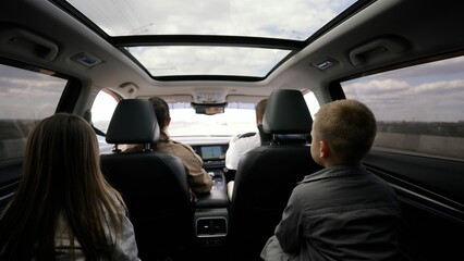 Fototapeta premium Family road trip scene featuring parents driving on highway with children gazing out backseat window, capturing moments of family togetherness and childhood adventure