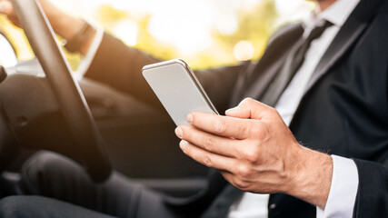 Driving safety concept. Cropped of businessman driving car, using mobile phone, checking location of business meeting, side view, copy space. Unrecognizable man using smartphone while driving