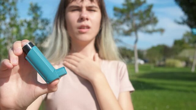 Asthma during summer weather. A view of asthmatic girl use her inhaler for breathing slowly in the sunny summer garden.