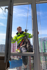 Man in Safety Gear Performing Window Cleaning from Height with Modern Equipment Against a Backdrop...